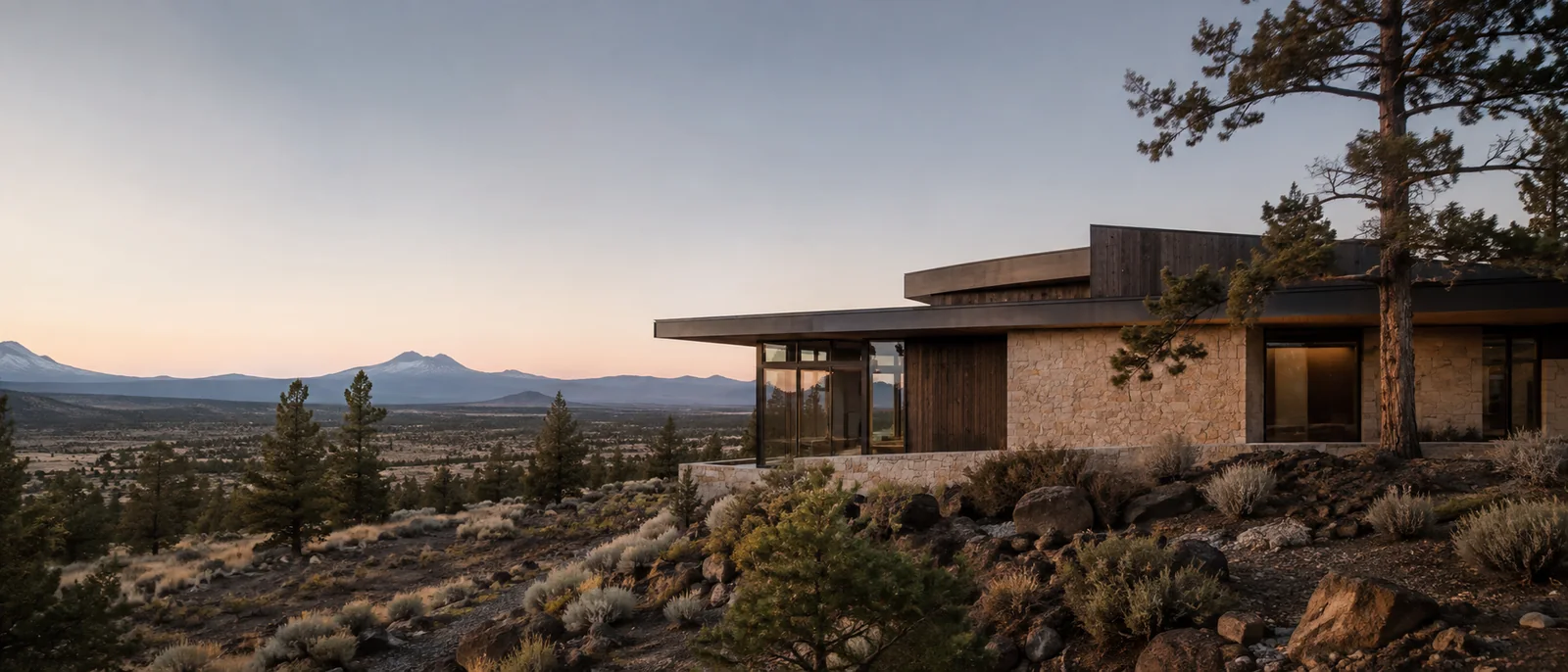 Restrained custom home integrated into a rocky Central Oregon high-desert landscape at dusk.